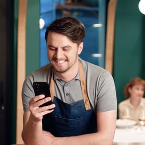 Merchant smiling while looking at phone in restaurant